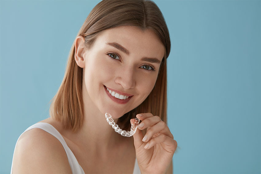 cute young woman placing clear braces on her top teeth